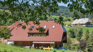 A large house with a red roof, a balcony, and a patio area with outdoor furniture. - Holiday Apartment Tannenblick (Hinterzarten)