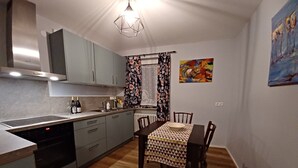 A compact kitchen with modern appliances, a dining table with chairs, and a window with patterned curtains.