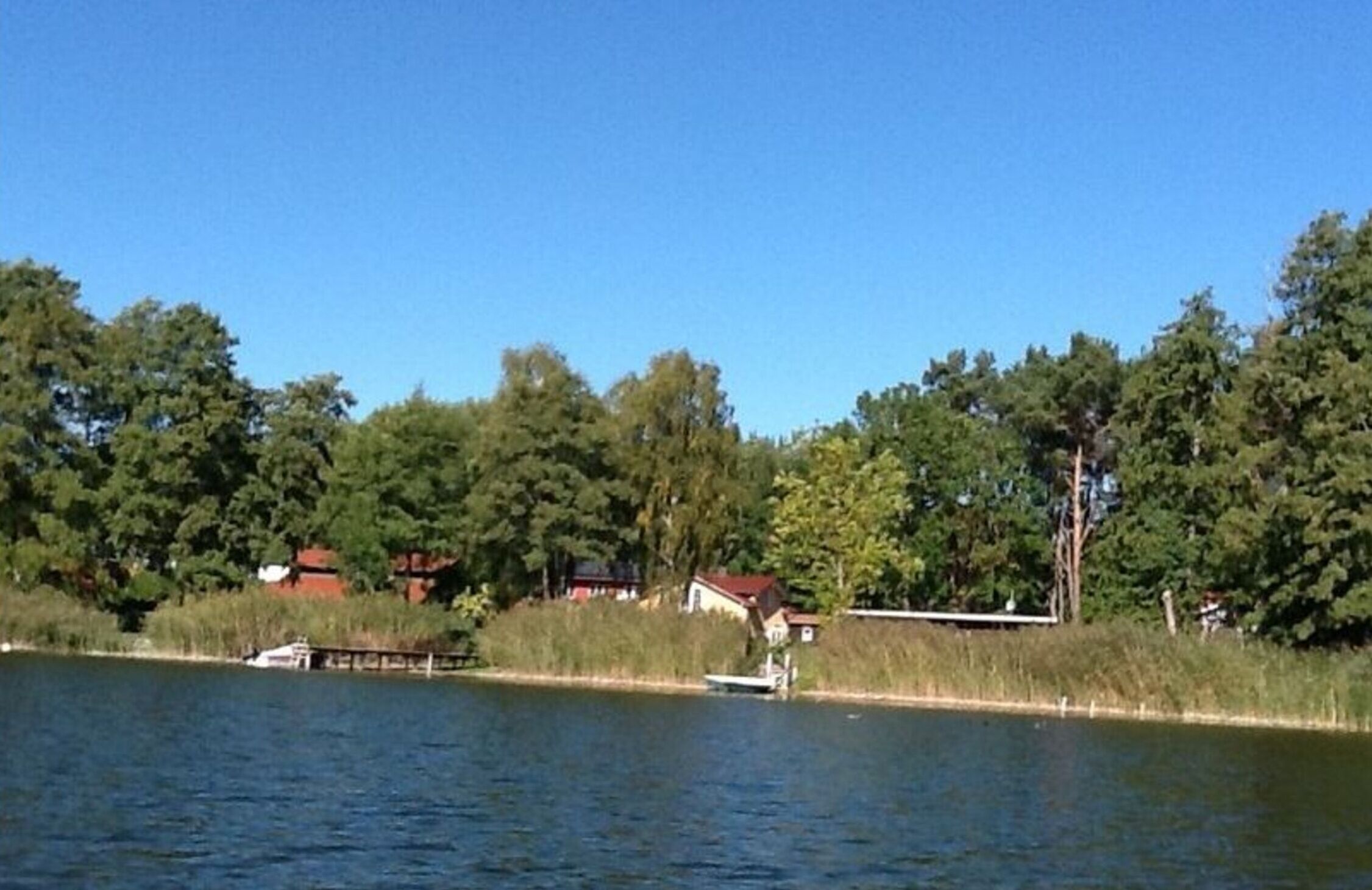 Blick auf einen See mit Häusern und einem Steg.