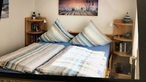A bedroom with a bed, striped pillows, a nightstand, a bookshelf, and a painting of a sunset over water. - Holiday Home Lalelu Comfortable Vacation Home (Jabel)
