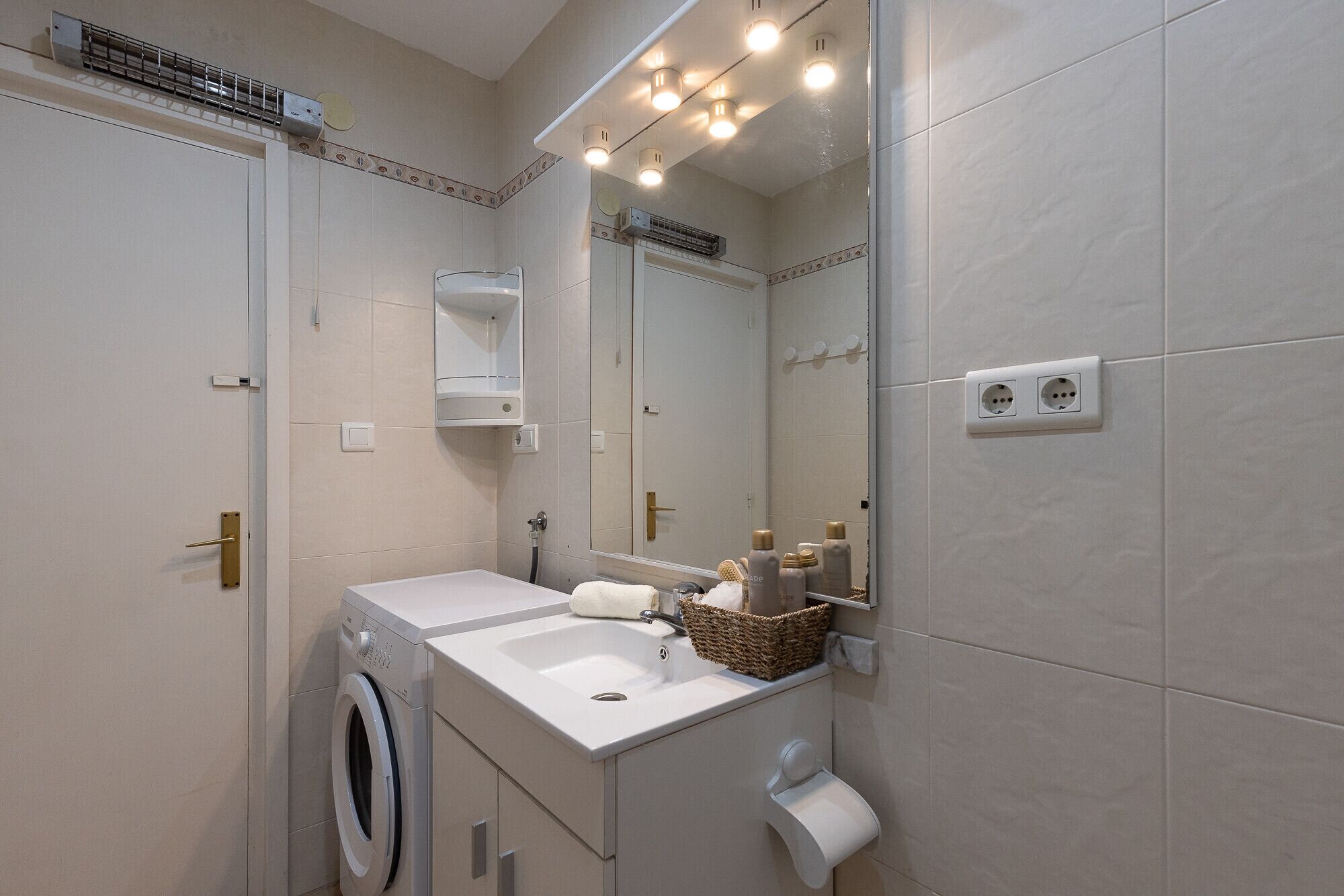 A modern bathroom with a built-in washing machine, a sink, and a mirror.