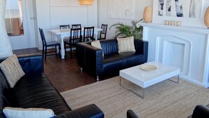 A modern living room with a black leather sofa, a white coffee table, and a dining area with a white table and chairs. - Nieuwpoort Central Retreat (Nieuwpoort)