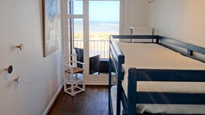 A room with a bunk bed, a chair, a small table, and a view of the beach through a glass door. - Nieuwpoort Central Retreat (Nieuwpoort)