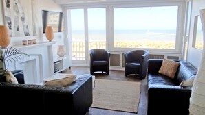 A modern living room with a large window overlooking a beach, furnished with black leather sofas and armchairs, a fireplace, and a flat-screen TV. - Nieuwpoort Central Retreat (Nieuwpoort)