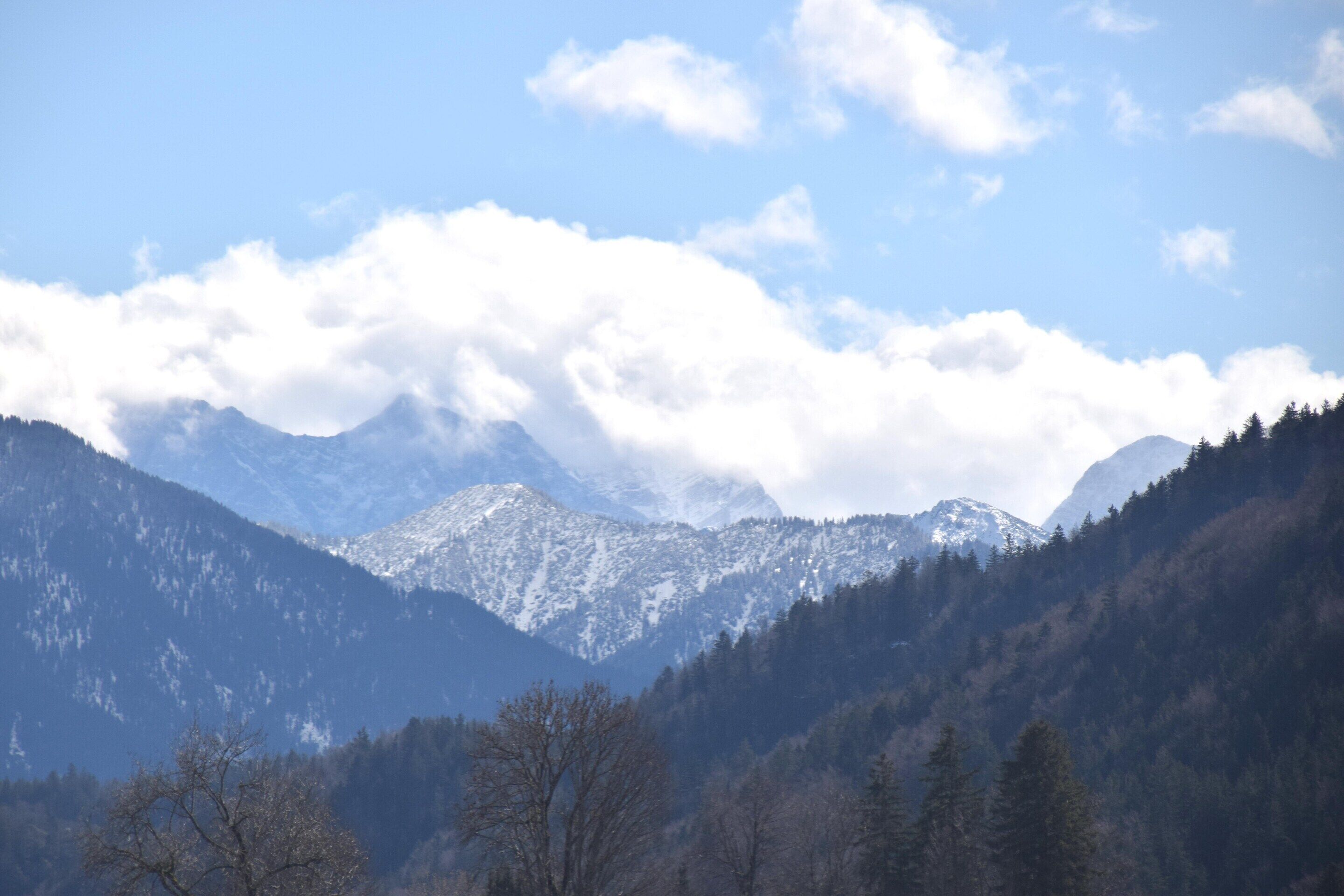 Un paysage montagneux avec des sommets enneigés et une vallée boisée.