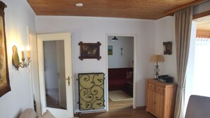 A living room with a beige sofa, a wooden cabinet, a lamp, and a door leading to another room. - Ferienhaus im Malerischen Allgau (Fuessen)
