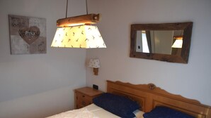 A double bed with white and blue bedding, a wooden headboard, a bedside table with a lamp, and a wall-mounted mirror. - Ferienhaus im Malerischen Allgau (Fuessen)