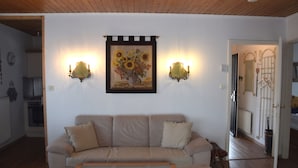 A living room with a beige sofa, a coffee table, and a painting of sunflowers on the wall. - Ferienhaus im Malerischen Allgau (Fuessen)