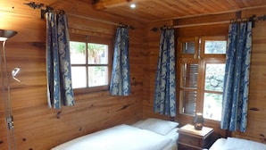 A wooden cabin room with two single beds, a nightstand, a lamp, and curtains on the windows. - Holiday Home Finca (Icod de los Vinos)