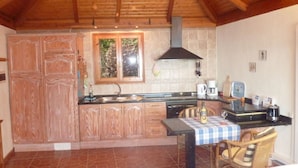 A compact kitchen with wooden cabinets, a gas stove, and a window overlooking greenery. - Holiday Home Finca (Icod de los Vinos)