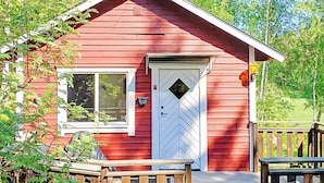 A red wooden cabin with a white door, a window, and a small porch with a bench.