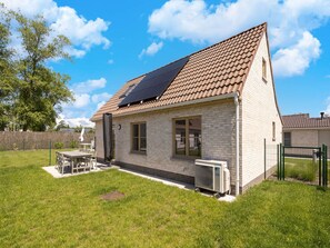 Une maison de plain-pied avec un toit en tuiles, une façade en briques et un petit patio comprenant une table et des chaises.