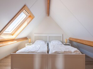 Une chambre avec un plafond en pente, une lucarne et un lit avec deux tables de chevet.