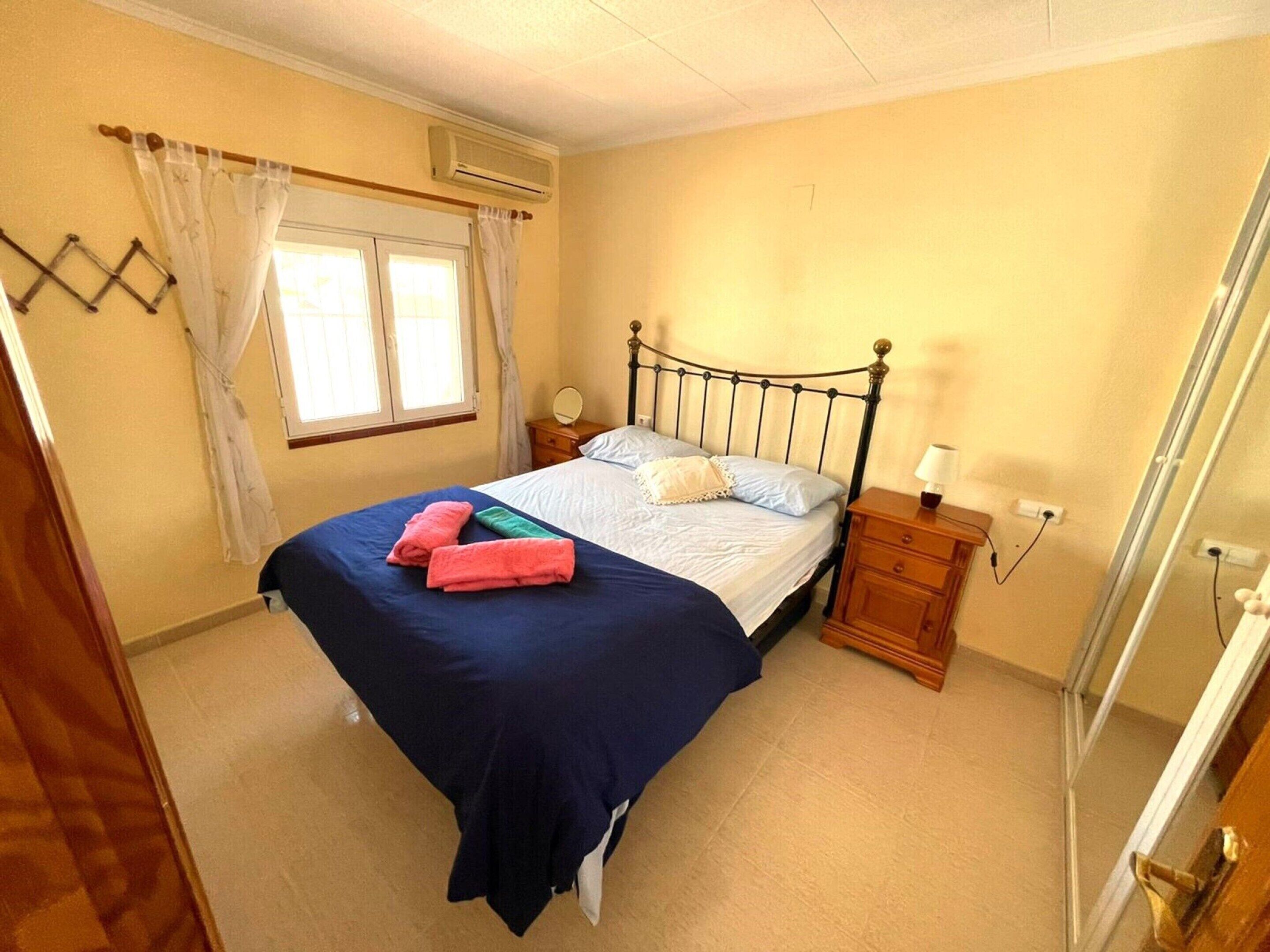 Een slaapkamer met een bed, nachtkastje en gordijnen voor het raam.