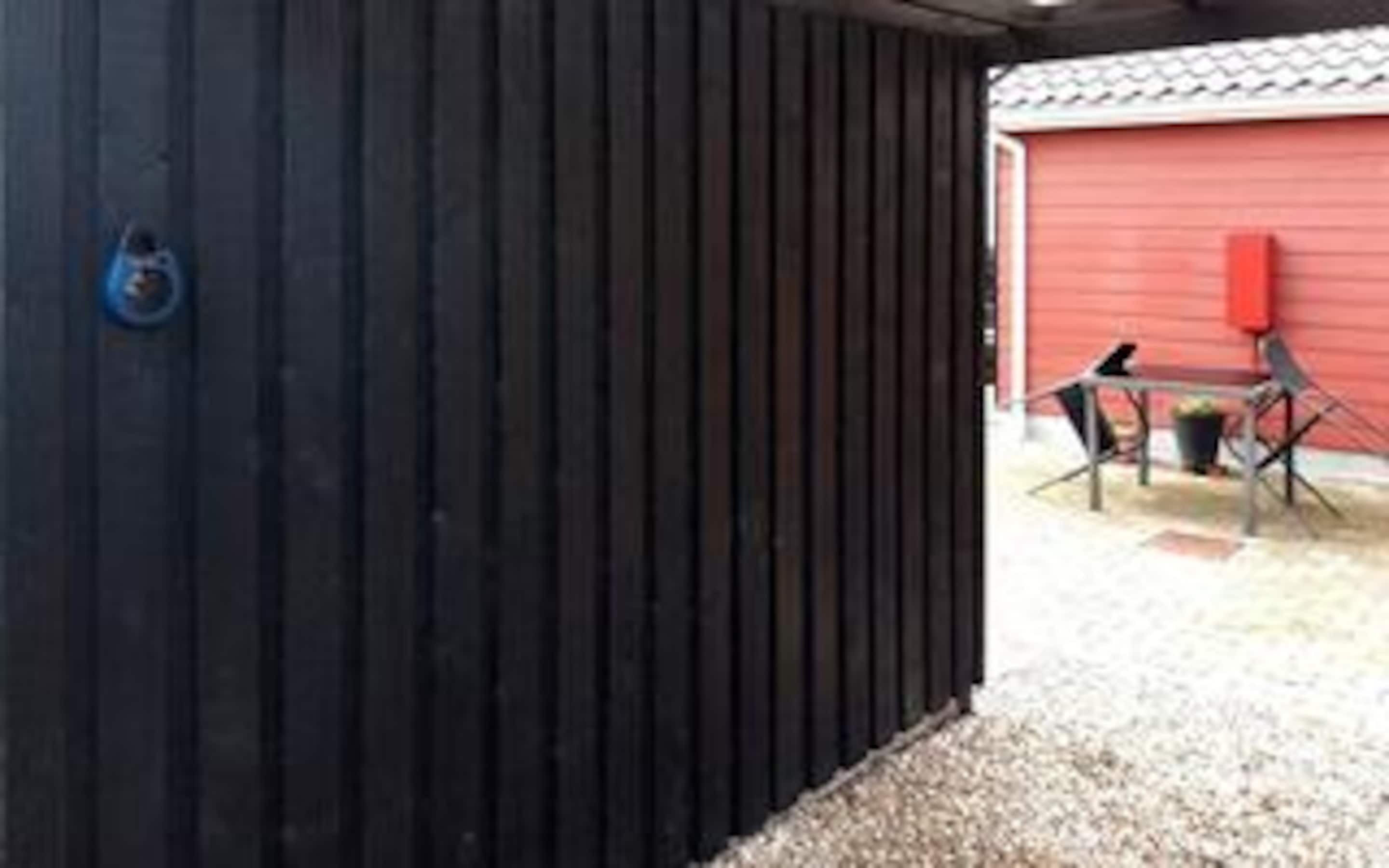 A black exterior wall of a building with a red door and a small outdoor seating area with a table and chairs.