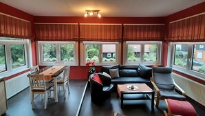 Una sala de estar moderna con comedor, ventanas amplias con cortinas, un sofá negro y una mesita pequeña.
