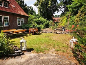 A backyard with a brick house, a wooden bench, a picnic table, and two lanterns.