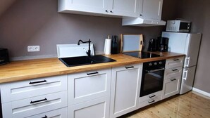 A modern kitchen with white cabinets, a wooden countertop, a black sink, and a built-in oven. - Sophienhof Lieselotte (Neuenkirchen)