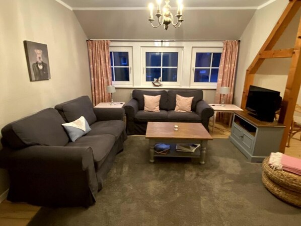 A living room with two sofas, a coffee table, a TV, and a chandelier.
