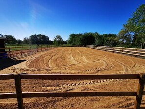 A dirt riding arena with a wooden fence and a clear sky.