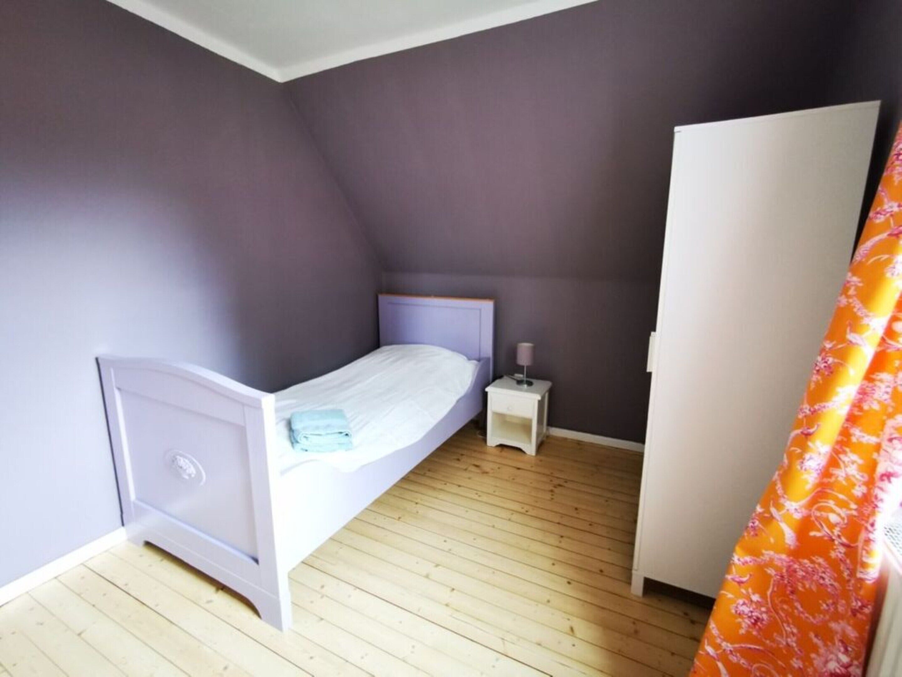 Ein kleines Schlafzimmer mit einem Einzelbett, einem Nachttisch, einem Kleiderschrank und einem Vorhang.