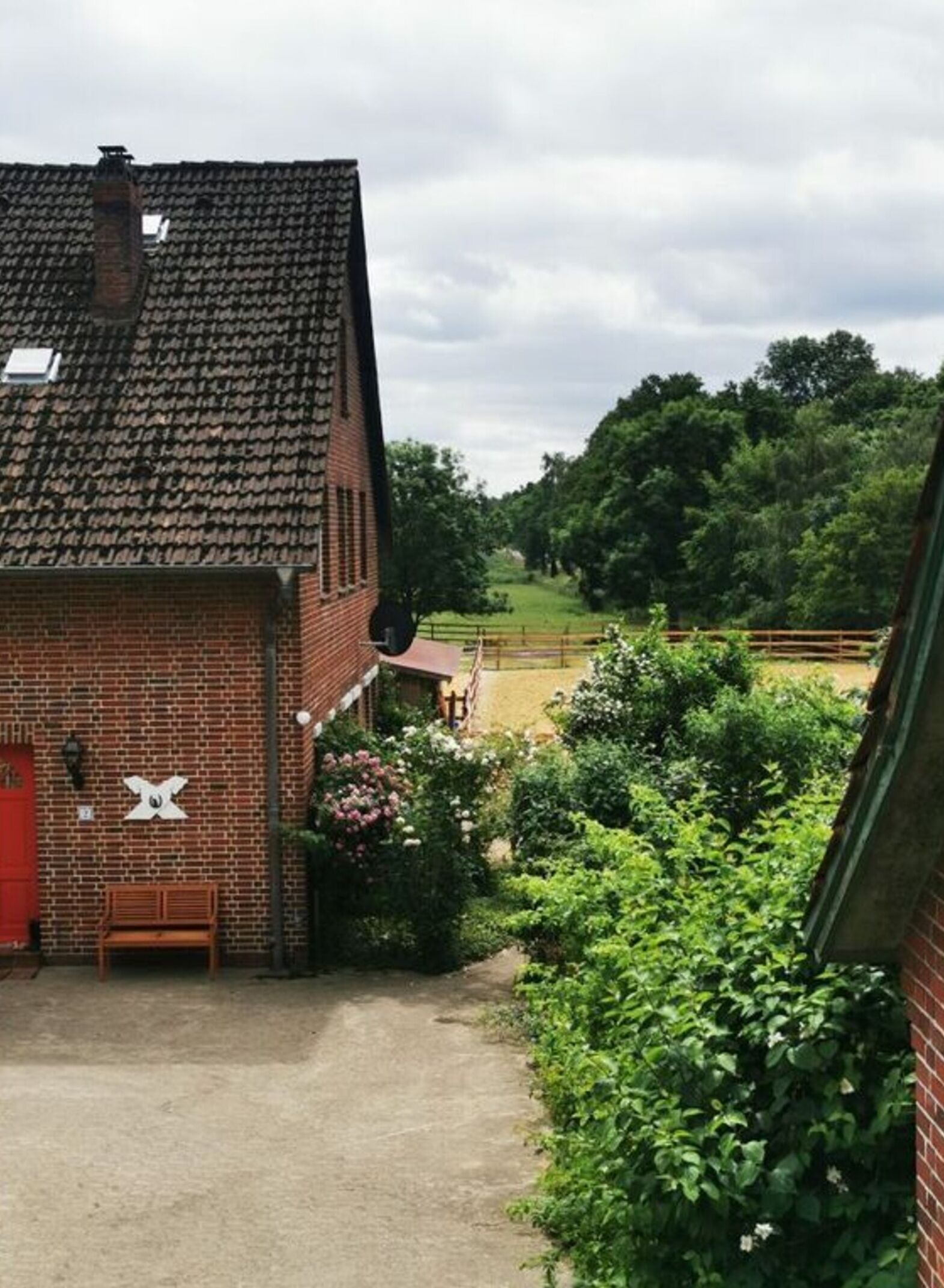A brick building with a red door, a bench, and a garden with flowers and bushes.