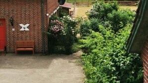 A brick building with a red door, a bench, and a garden with flowers and bushes. - Sophienhof Lieselotte (Neuenkirchen)
