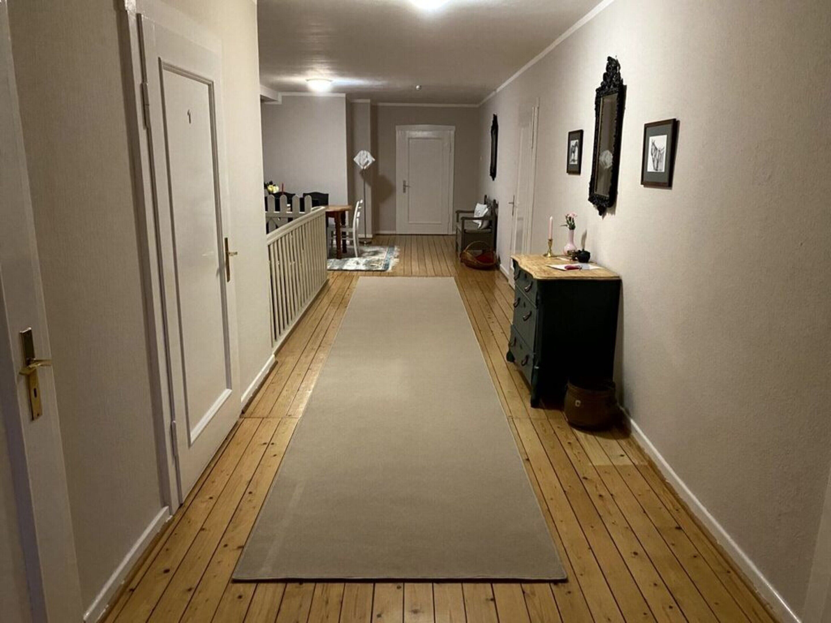 A narrow hallway with wooden flooring, a beige carpet, and a dresser with drawers.