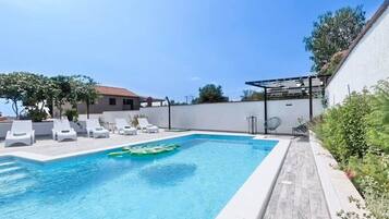 A swimming pool with lounge chairs, a pergola, and a white wall.