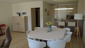 Un comedor con una mesa redonda, sillas blancas, un jarrón con flores y una lámpara.