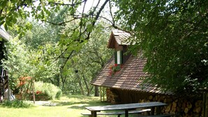 A rustic wooden cabin with a thatched roof, surrounded by lush greenery and a picnic table in the foreground. - The Holler Comfortable Holiday Residence (Schwanberg)