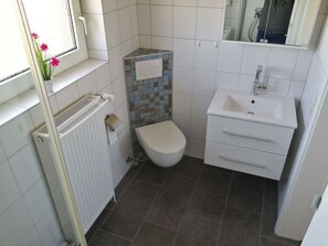 A small bathroom with a toilet, a sink, and a window with flowers. - Baudewig Modern Retreat (Nordstrand)