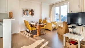 Ein modernes Wohnzimmer mit Essbereich, einem Flachbildfernseher und einem großen Fenster mit Blick auf die Stadt.