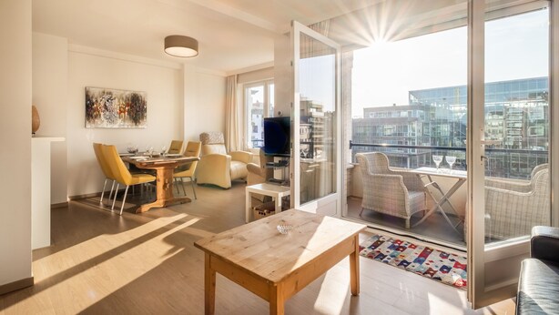Ein modernes Wohnzimmer mit Essbereich, Fernseher und einem Balkon mit Blick auf die Stadt.
