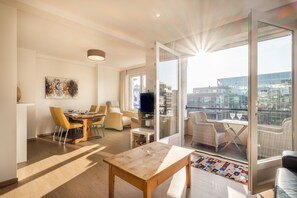 A modern living room with a dining area, a TV, and a balcony with city views. - Apartment in Koksijde With Side Sea View (Koksijde)