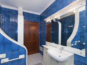 A bathroom with blue tiles, a wooden door, a white sink, and a mirror.