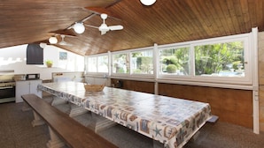 A kitchen with a long island counter, wooden ceiling, and large windows with a view of greenery. - Topazio Comfortable Holiday Residence (Quartu Sant'Elena)