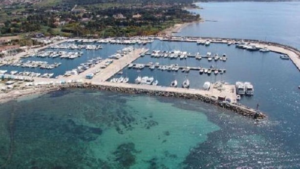 An aerial view of a marina with numerous boats docked, surrounded by clear water and a hilly landscape in the background. - Topazio Comfortable Holiday Residence (Quartu Sant'Elena)