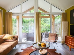Un salon spacieux doté d’une grande porte-fenêtre coulissante donnant sur une terrasse, d’un canapé, d’un fauteuil, d’une table basse agrémentée d’objets décoratifs et d’un téléviseur.