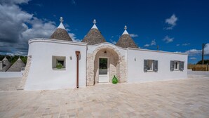 A building with a white facade, three conical roofs, and a stone archway entrance. - Villa 'I Trulli Di Ninì' with Private Pool, Wi-Fi and Air Conditioning (martina franca)