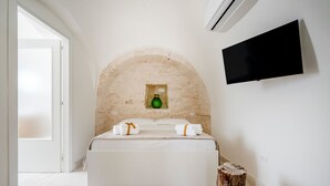 A bedroom with a stone arch, a bed, a flat-screen TV, and a wooden stump. - Villa 'I Trulli Di Ninì' with Private Pool, Wi-Fi and Air Conditioning (martina franca)