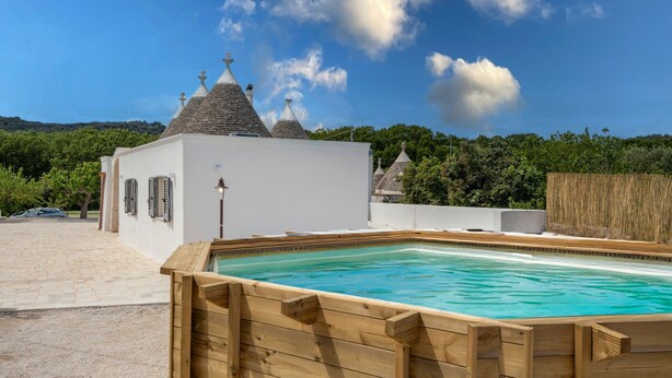 A swimming pool with a wooden deck, a white building with a tiled roof, and a clear blue sky. - Villa 'I Trulli Di Ninì' with Private Pool, Wi-Fi and Air Conditioning (martina franca)
