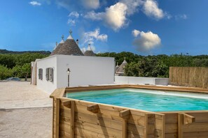Ein Schwimmbecken mit Holzterrasse, ein weißes Gebäude mit einem Ziegeldach und einem strahlend blauen Himmel.