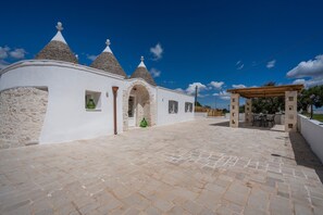 A white building with conical roofs, a paved courtyard, and a wooden pergola.