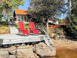 Een houten terras met rode stoelen en een leuning, met uitzicht op een rotsachtig gebied en een gebouw met een rood dak.