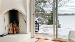 A room with a fireplace, a white rug, and a view of a snowy landscape through a glass door. - 2 Person Holiday Home in Bello (Hjältevad)