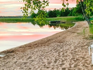 Een zandstrand met een boot afgemeerd in het water, omgeven door begroeiing en bomen.