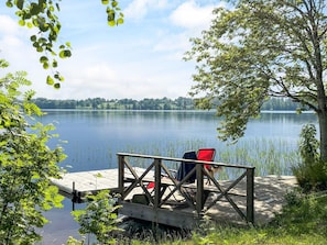 Een houten steiger met een stoel en een rode tas, met uitzicht op een kalm meer met een bebost oever.