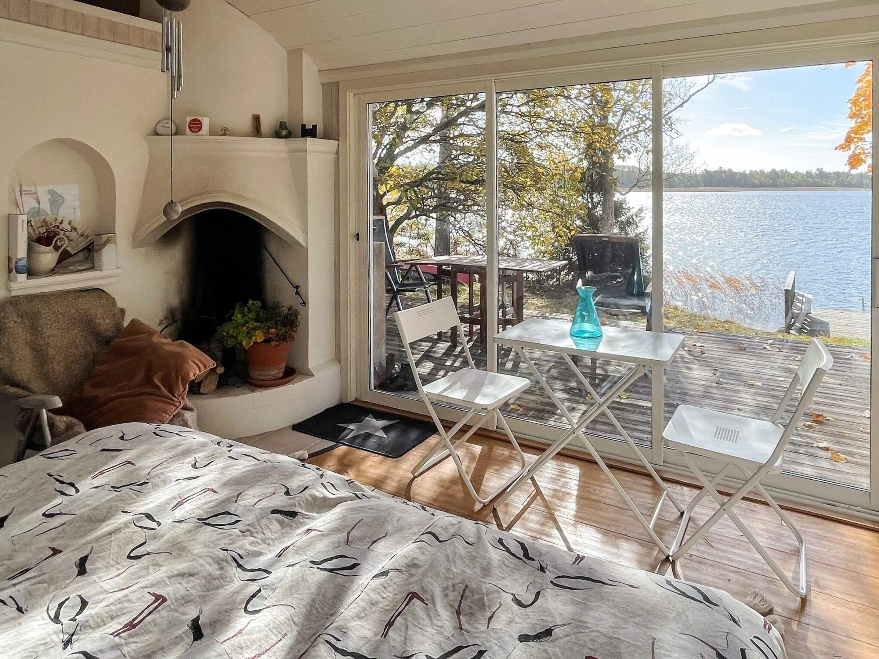 Un'accogliente camera da letto con camino, un letto con copriletto fantasia, un tavolino con sedie e una grande finestra vista lago.