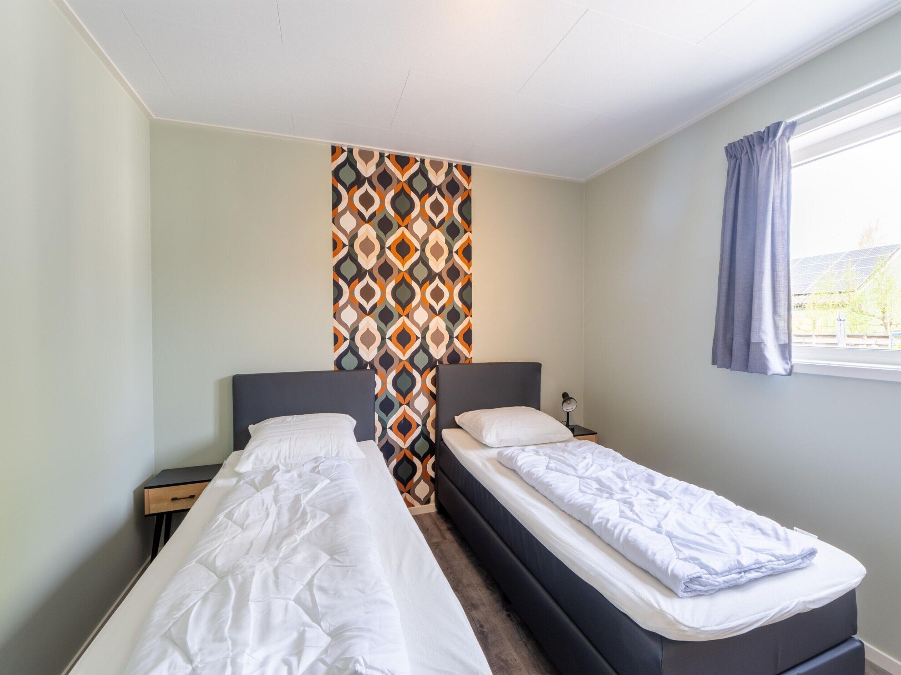A room with two single beds, a small bedside table with a lamp, and a window with curtains.